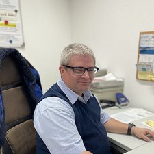 Ein lächelnder Mann am Schreibtisch bei der Arbeit Ein Mann mit grauen Haaren und Brille sitzt an einem Schreibtisch, lächelt und wirkt entspannt in einem Büro.